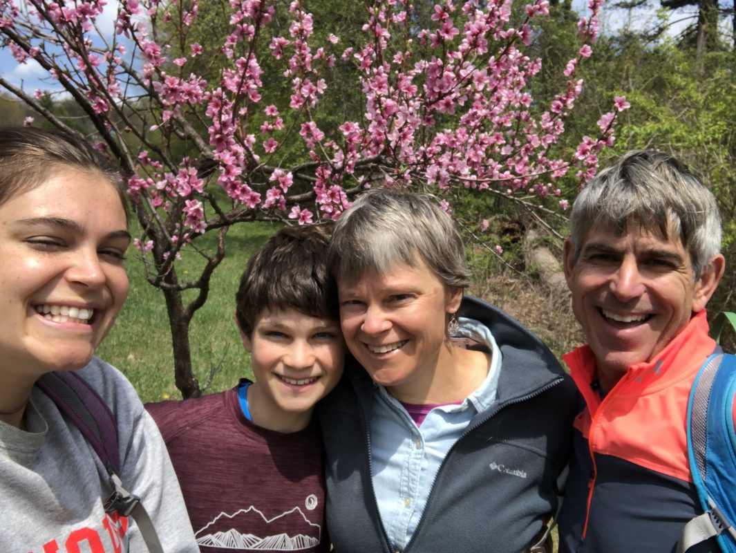 Sally, her husband, and two of her kids in front of a tree with pink blossoms on a recent hike