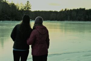 A pair of friends stand in front of a frozen lake as the sun sets.