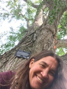 Gaby looking down into the camera and smiling, beneath an old Ginkgo tree at Smith College