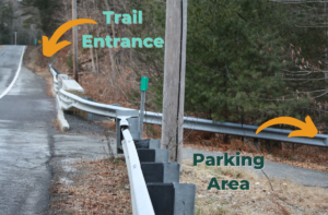 Photo shows the east side of Route 112 looking North from just south of the parking area. Text reading "parking area" accompanies an arrow pointing to the right and bottom of the image, while text reading "trail entrance" accompanies an arrow pointing in the upper left portion of the image.