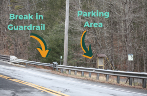 Photo of parking area as seen from across Route 112. Text reading "break in guardrail" accompanies an arrow pointing to the location. Text reading "parking area" accompanies an arrow pointing to the parking area. 