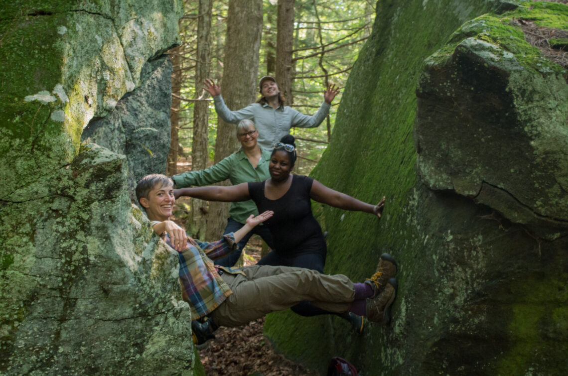 Smiling and wedged in various poses between two halves of a boulder are Katie, Tiffany, Sally, and Tim.