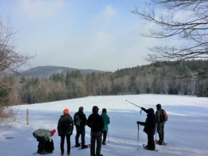 A group of snowshoers gaze at distant hills across a snowy field.