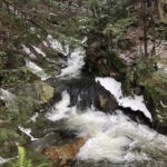 A photo of a small waterfall cascading through a wooded landscape.