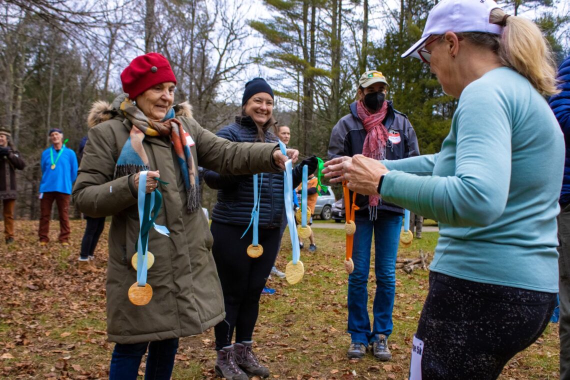 Three warmly dressed volunteers hand out cookie medals to 5k race finishers.