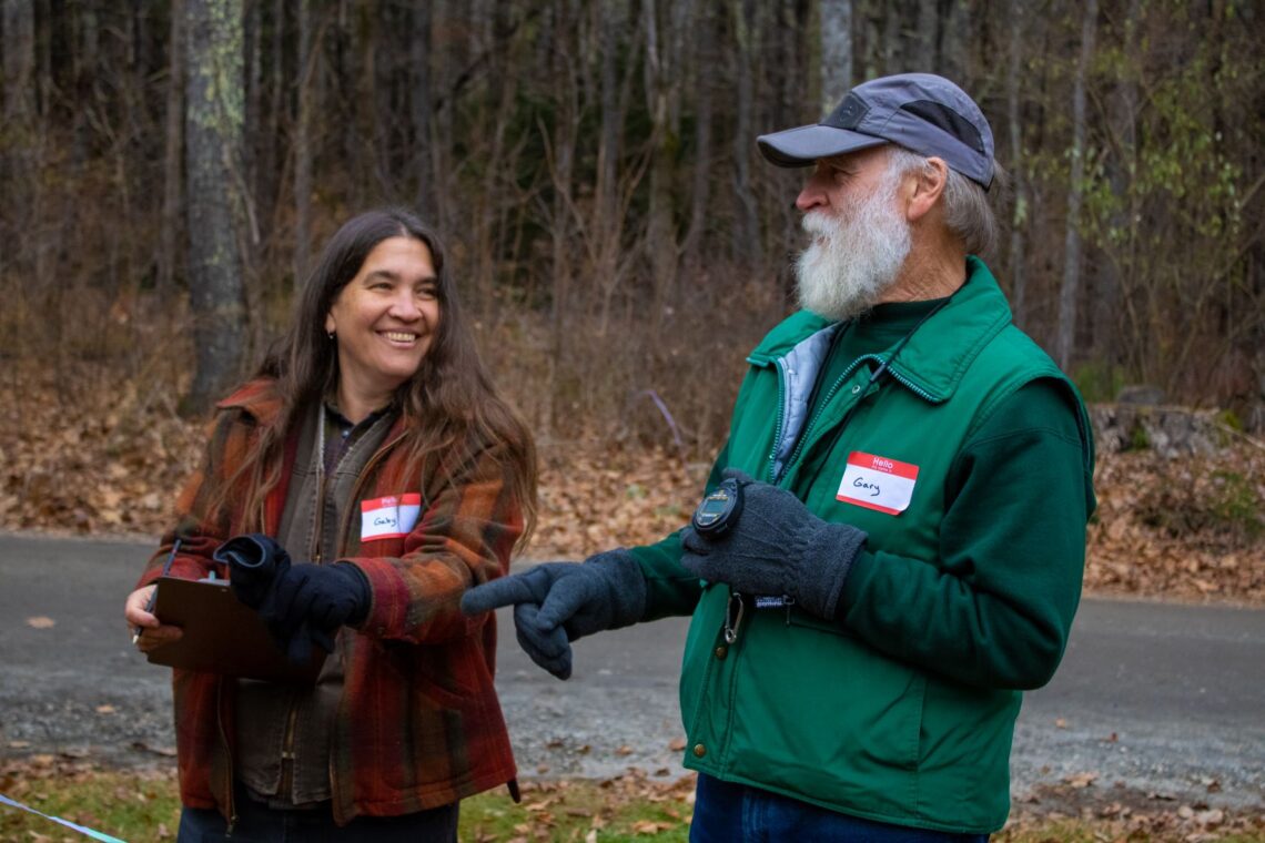 Two warmly dressed volunteers smile and laugh with each other on a late fall day.