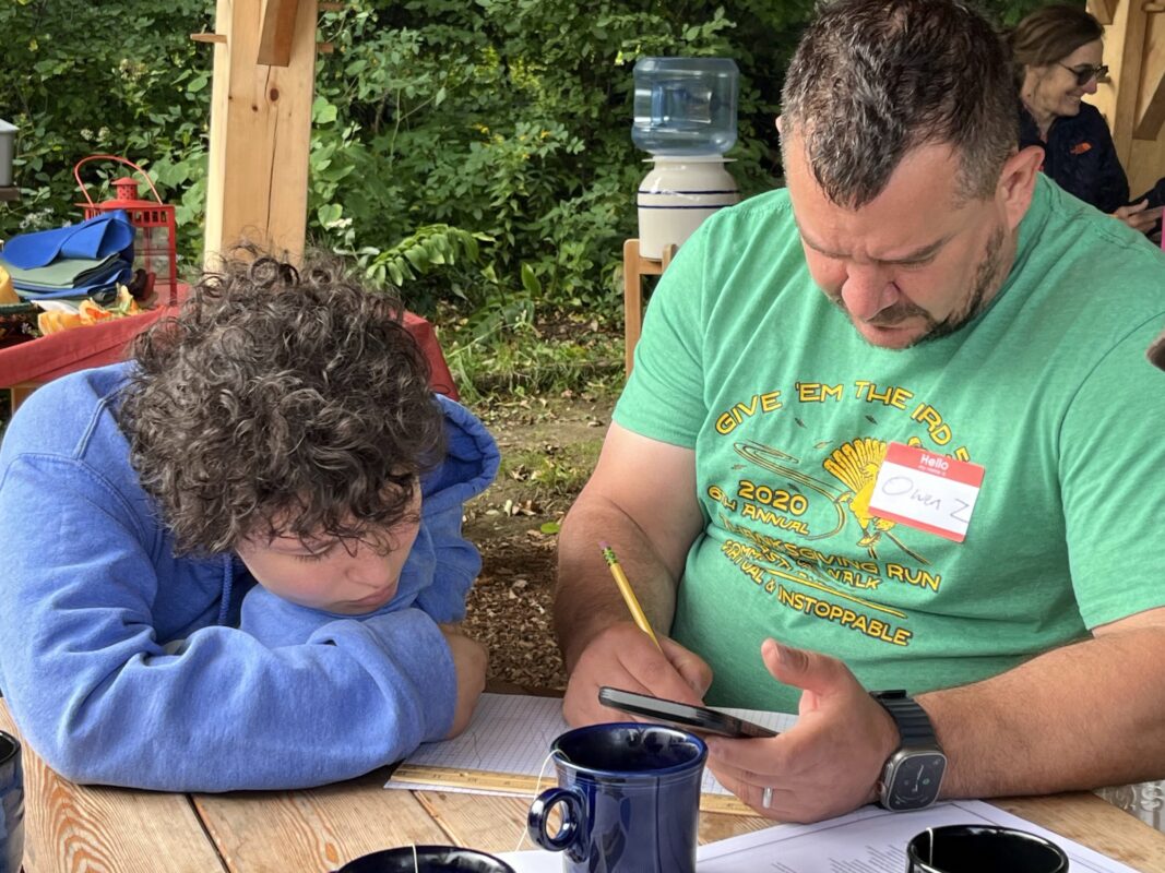 A zoomed-in image of Alex and Owen working on a drawing together while seated at a table.