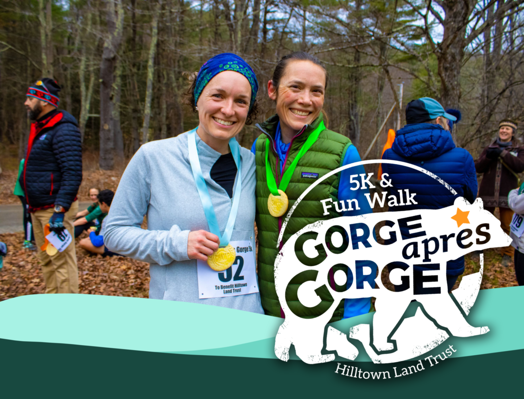 Framed by the hills of the HLT logo, two runners wearing warm clothes and cookie medals smile into the camera. The Gorge apres Gorge logo, a bear encircled with the text 5k and Fun Walk, Hilltown Land Trust, is overlaid in white.