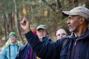 John holds up a leaf as a group of adult onlookers watches.