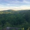 Last rays of light illuminate a green forested ridge as the sky turns from blue to yellow.
