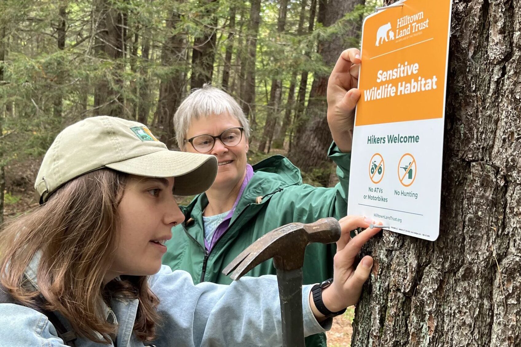 Mariel and Sally nail a Sensitive Wildlife Habitat sign to a tree.