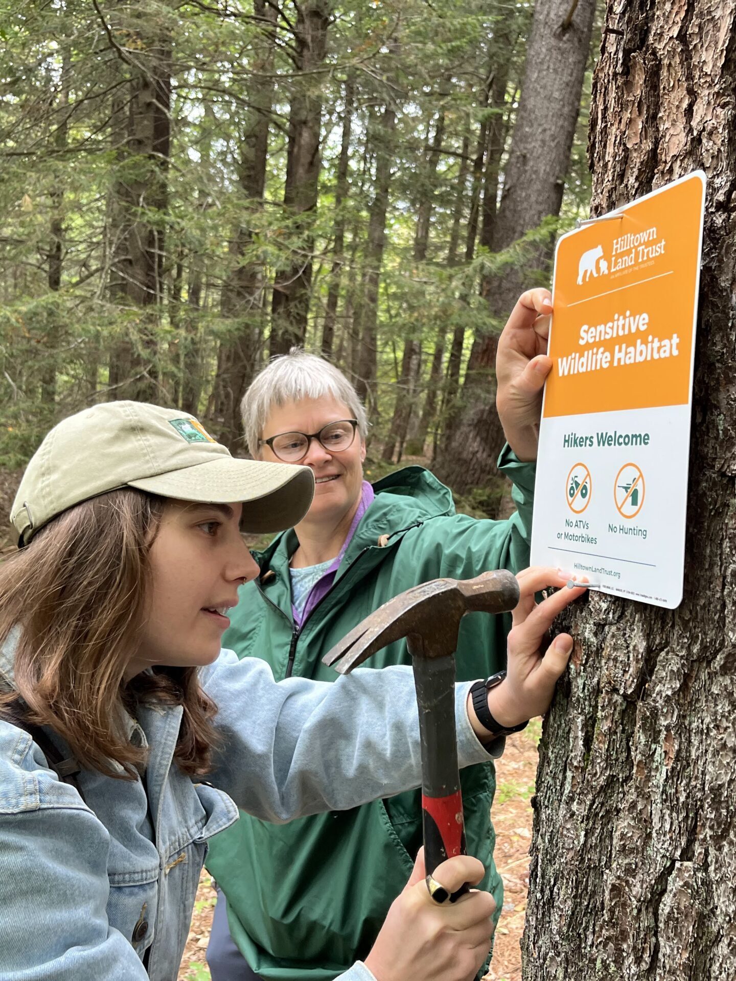 Mariel and Sally nail a Sensitive Wildlife Habitat sign to a tree.