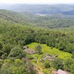 A bird's-eye photo of a lush green hilly landscape, with a bright green meadow in the center and blue hills stretching into the distance.