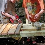 Two people work together to screw in planks onto a bridge.