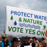 Banner that reads "Protect water & nature vote yes on 6" held above a crowd of people